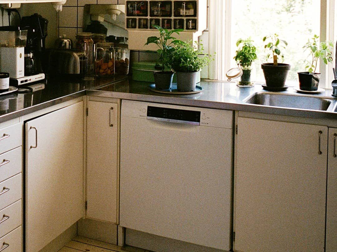 Ett kök med en diskmaskin. På diskbänken står flera krukor med örter.