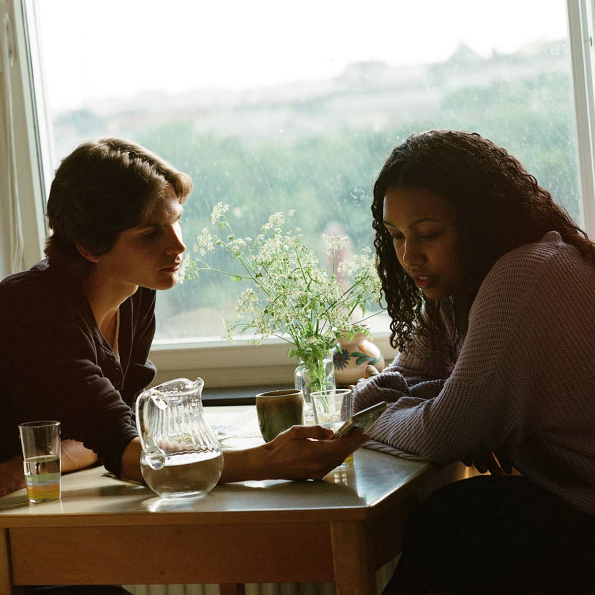 En person visar något på sin telefon för en annan vid ett köksbord