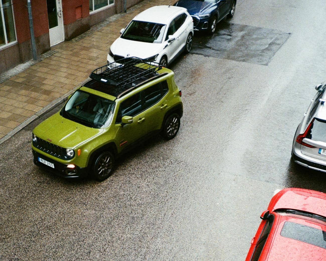 En grön bil fickparkerar på en gata och orsakar en parkeringsskada