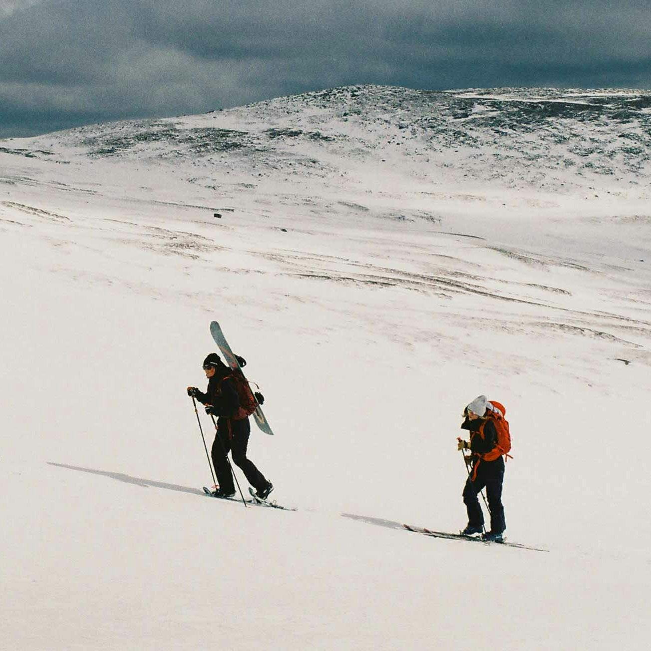 Två personer går på randonee-skidor uppför fjället.