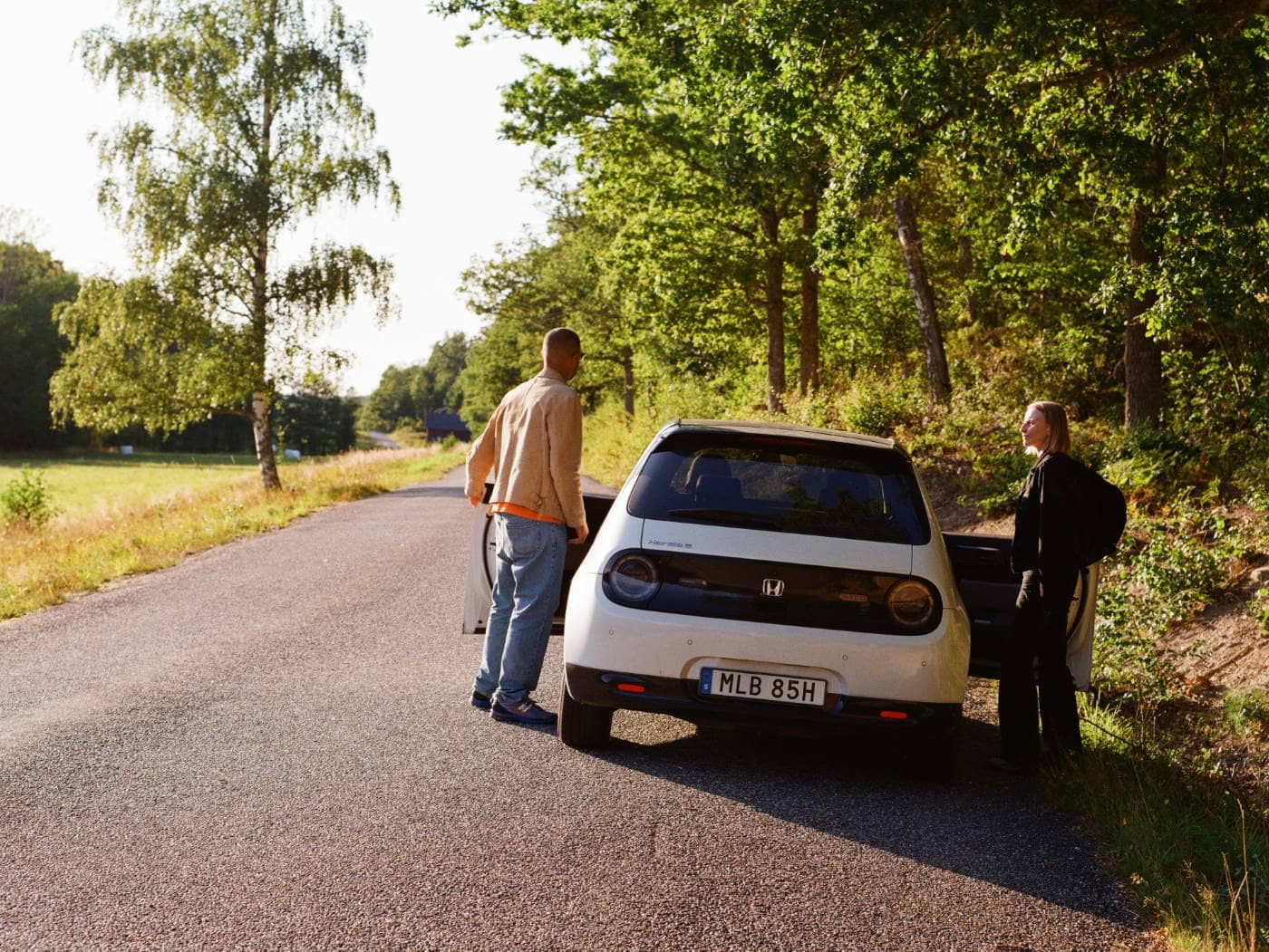 En vit bil som har stannat på en landsväg med två personer utanför