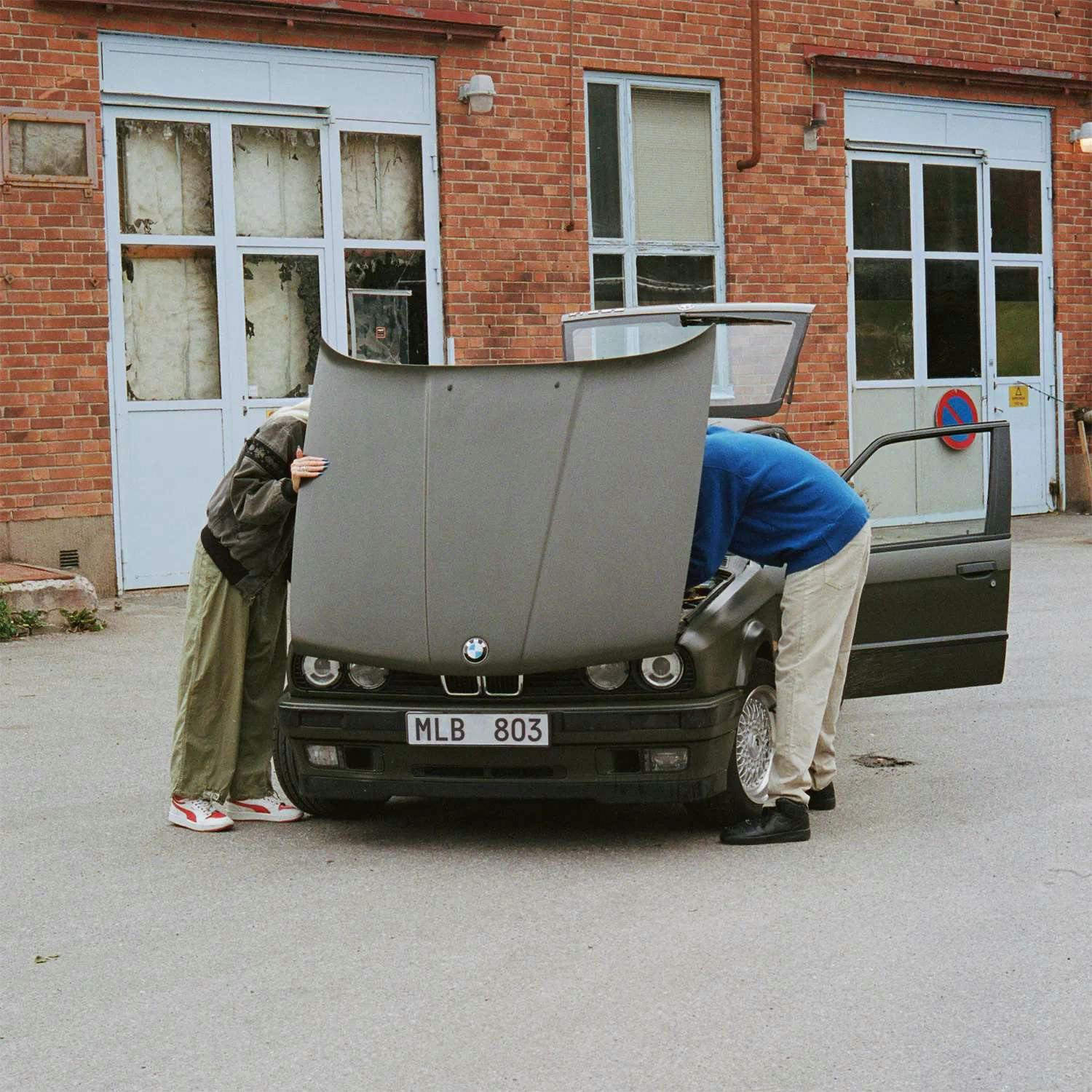 Bil med öppen motorhuv, som två personer försöker laga.